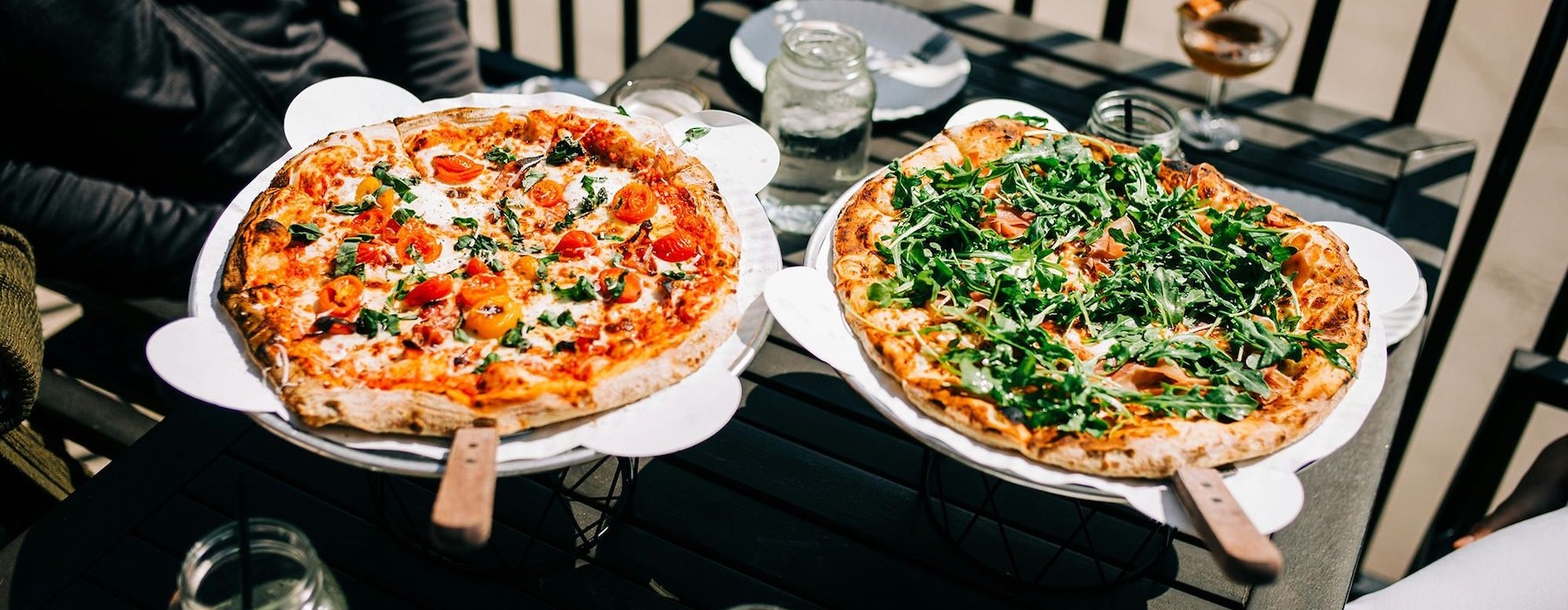 Two people with pizzas at a table outside.